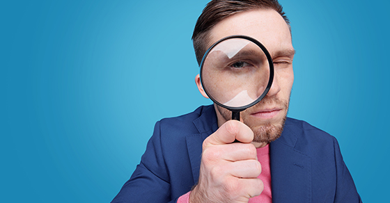 Serious young male detective holding magnifying glass by right eye Demo